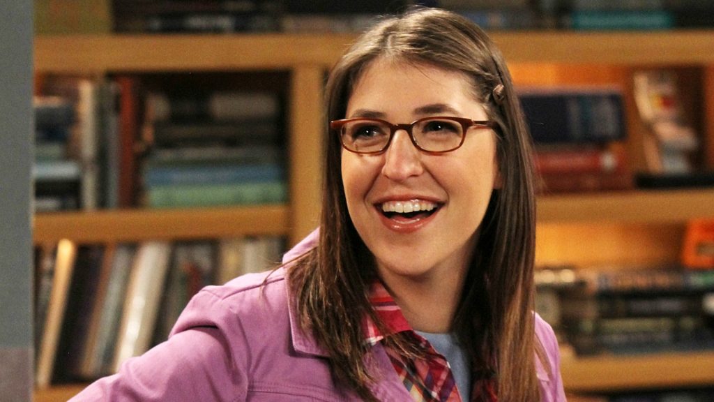 Amy smiles in the setting of The Big Bang Theory